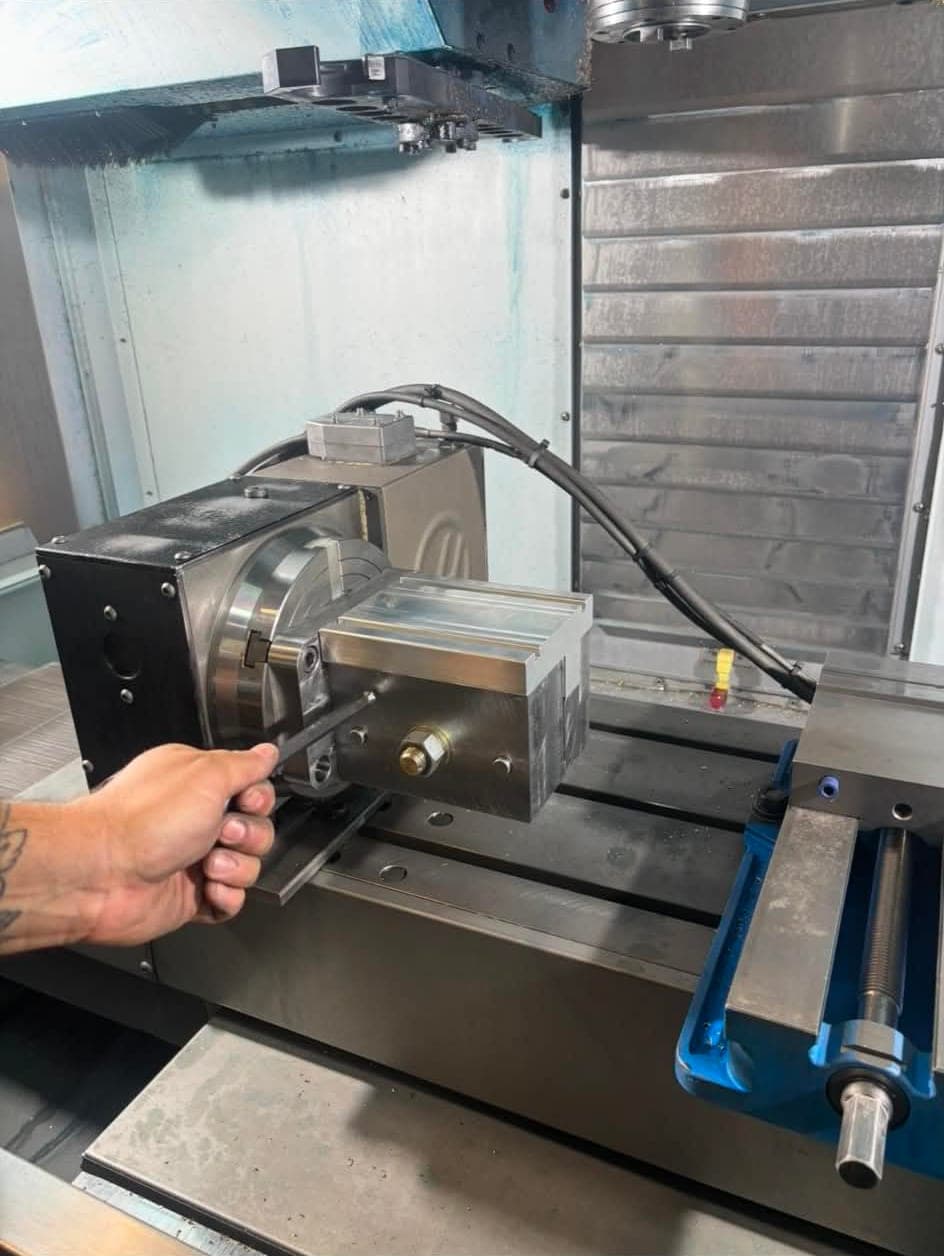 A rotary indexer and a machined workpiece set up on the table of a CNC machining center.