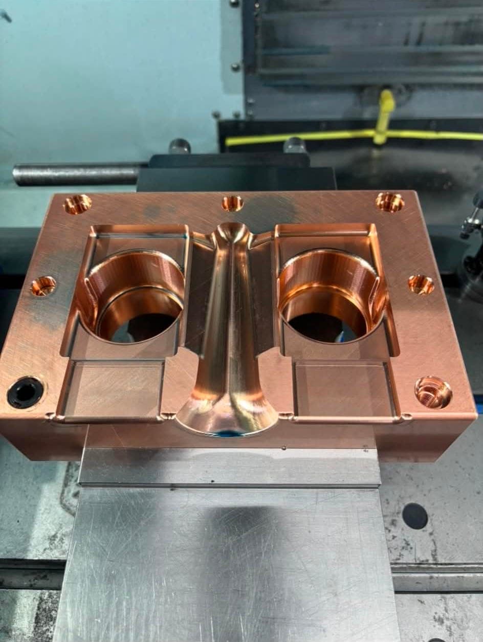 A machined mold block with twin cavities and a contoured center feature, still set up on the machine.